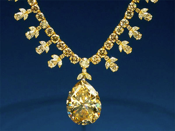 Close-up of an elegant yellow diamond necklace with a large pear-shaped diamond pendant and smaller round diamonds in a floral arrangement, set in a gold chain.