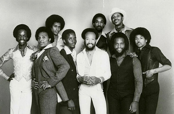 Black and white photo of the iconic 1970s music group Earth, Wind & Fire, featuring nine members in stylish vintage clothing and afro hairstyles.