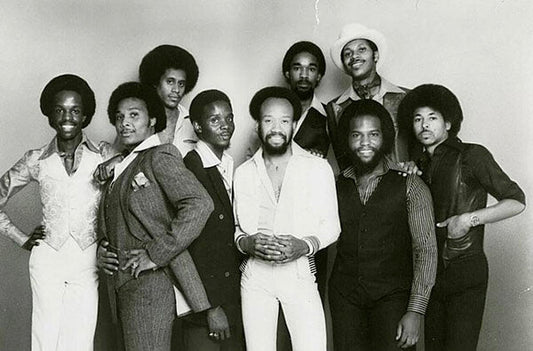 Black and white photo of the iconic 1970s music group Earth, Wind & Fire, featuring nine members in stylish vintage clothing and afro hairstyles.