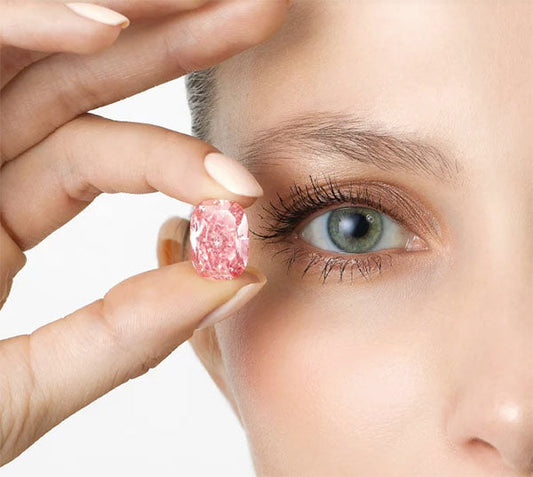 A close-up image of a woman holding a large pink diamond near her eye, highlighting the intricate details of the gemstone.